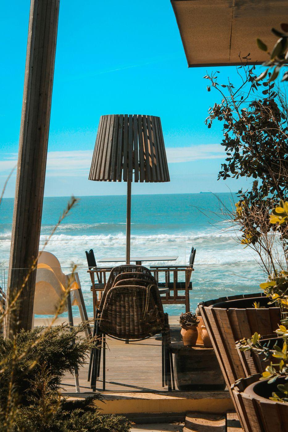 A seaside terrace with a wooden lamp and wicker chairs above a sunny beach