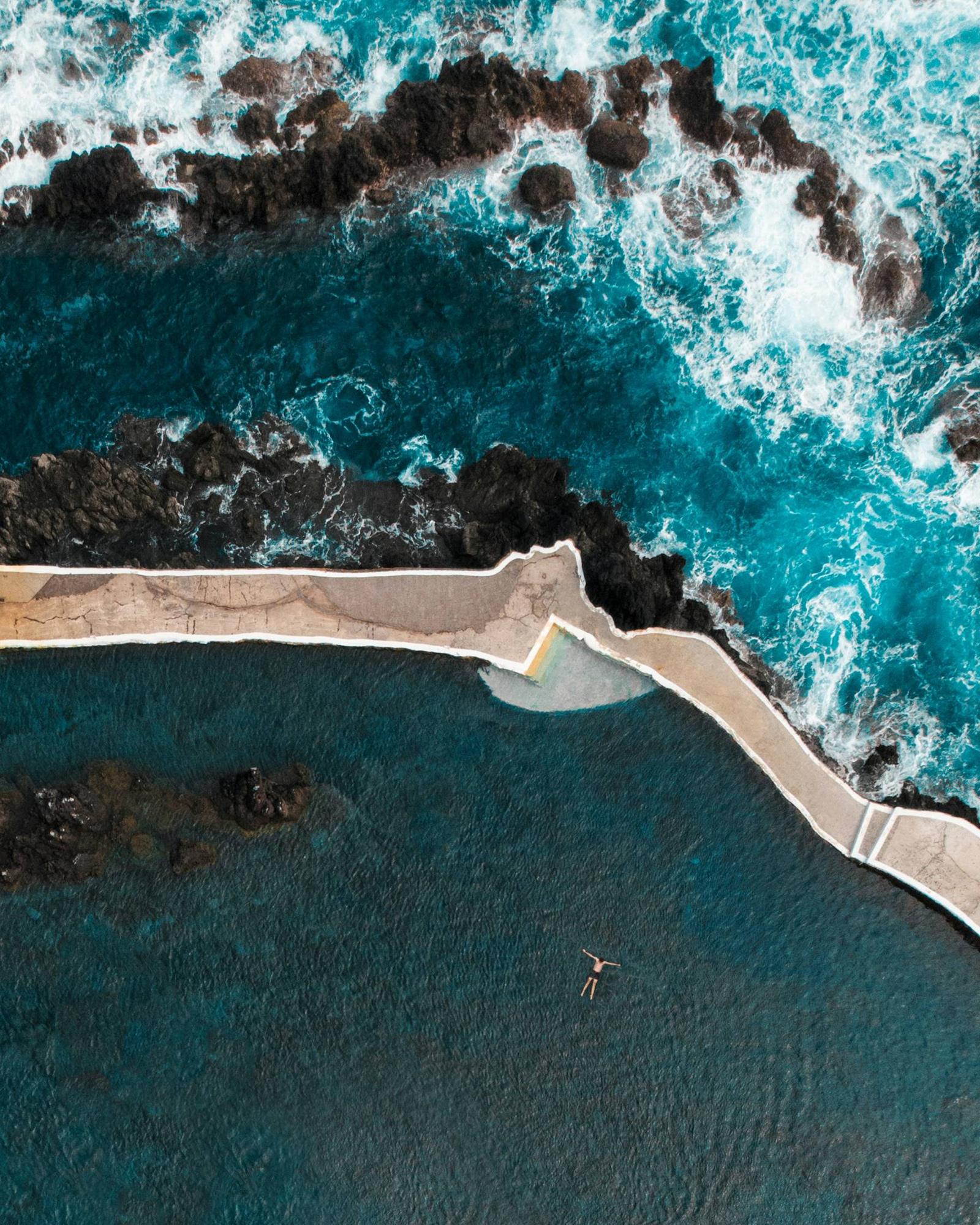 A lone swimmer floating in a natural ocean pool beside dark volcanic rocks