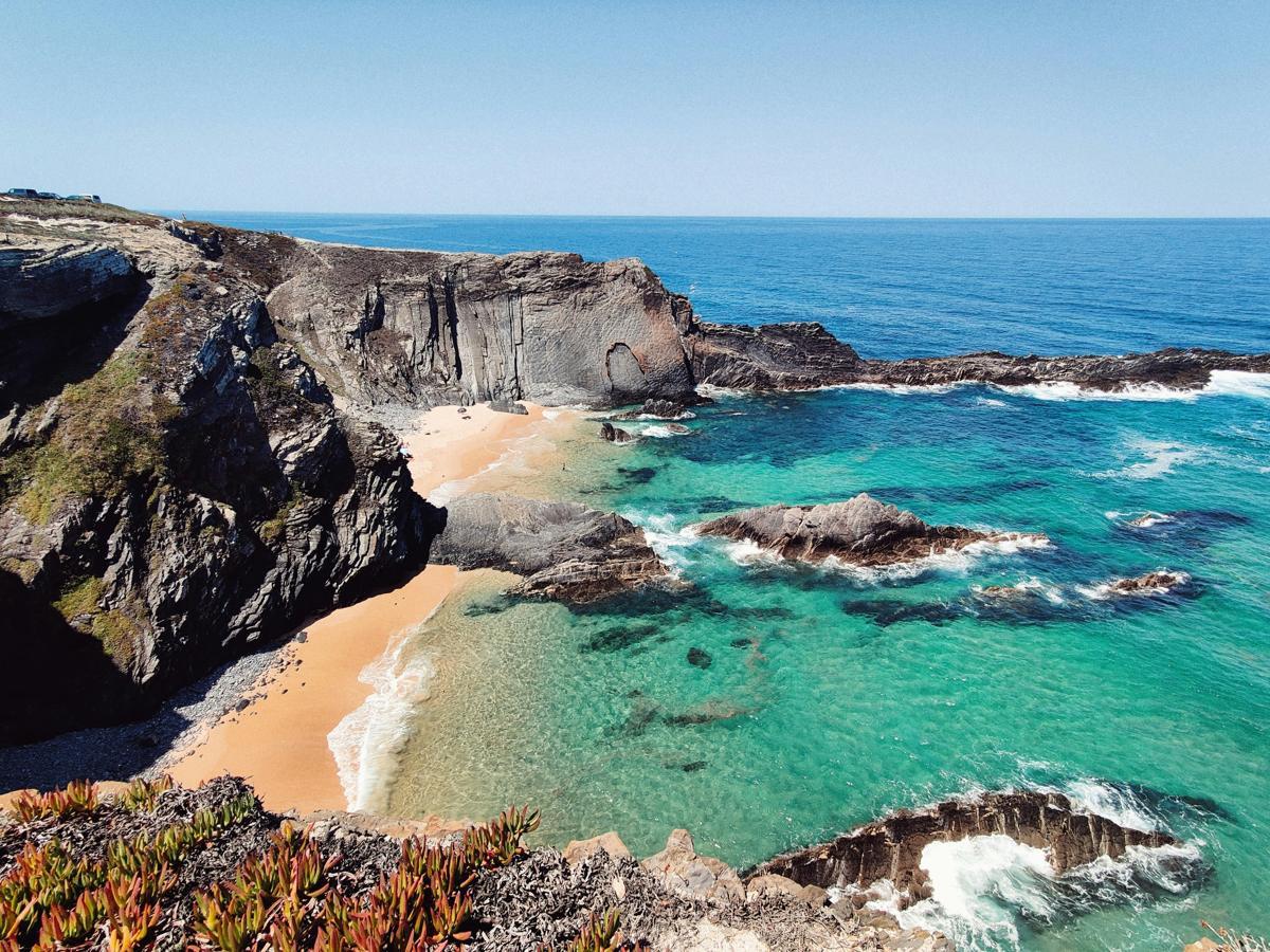 A quiet sandy cove below dark cliffs on Portugal&rsquo;s Alentejo coast