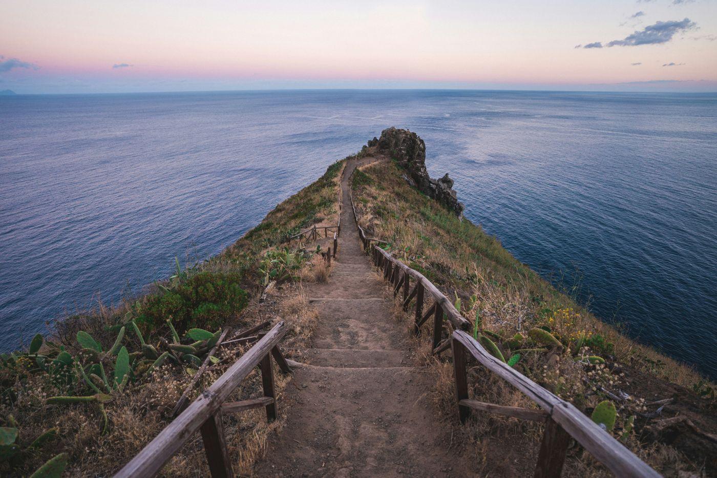 A fenced trail running out along a ridge to the open sea at dusk