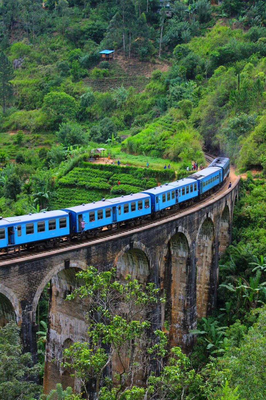 Blue train crossing a stone arch bridge through Sri Lanka&rsquo;s green hill country