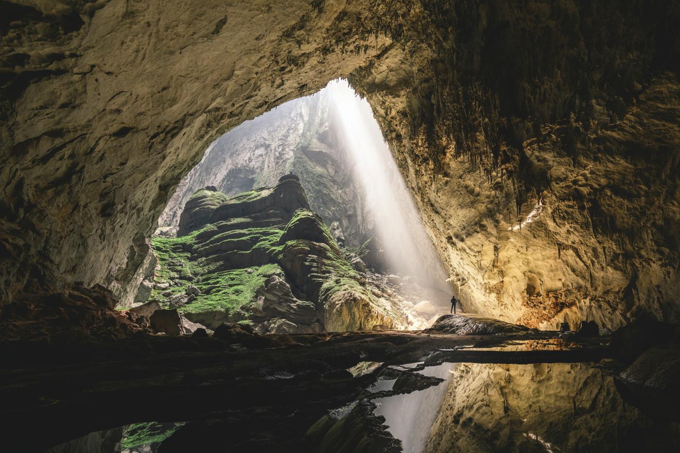 A lone figure in a vast cave lit by a shaft of sunlight in Phong Nha, Vietnam